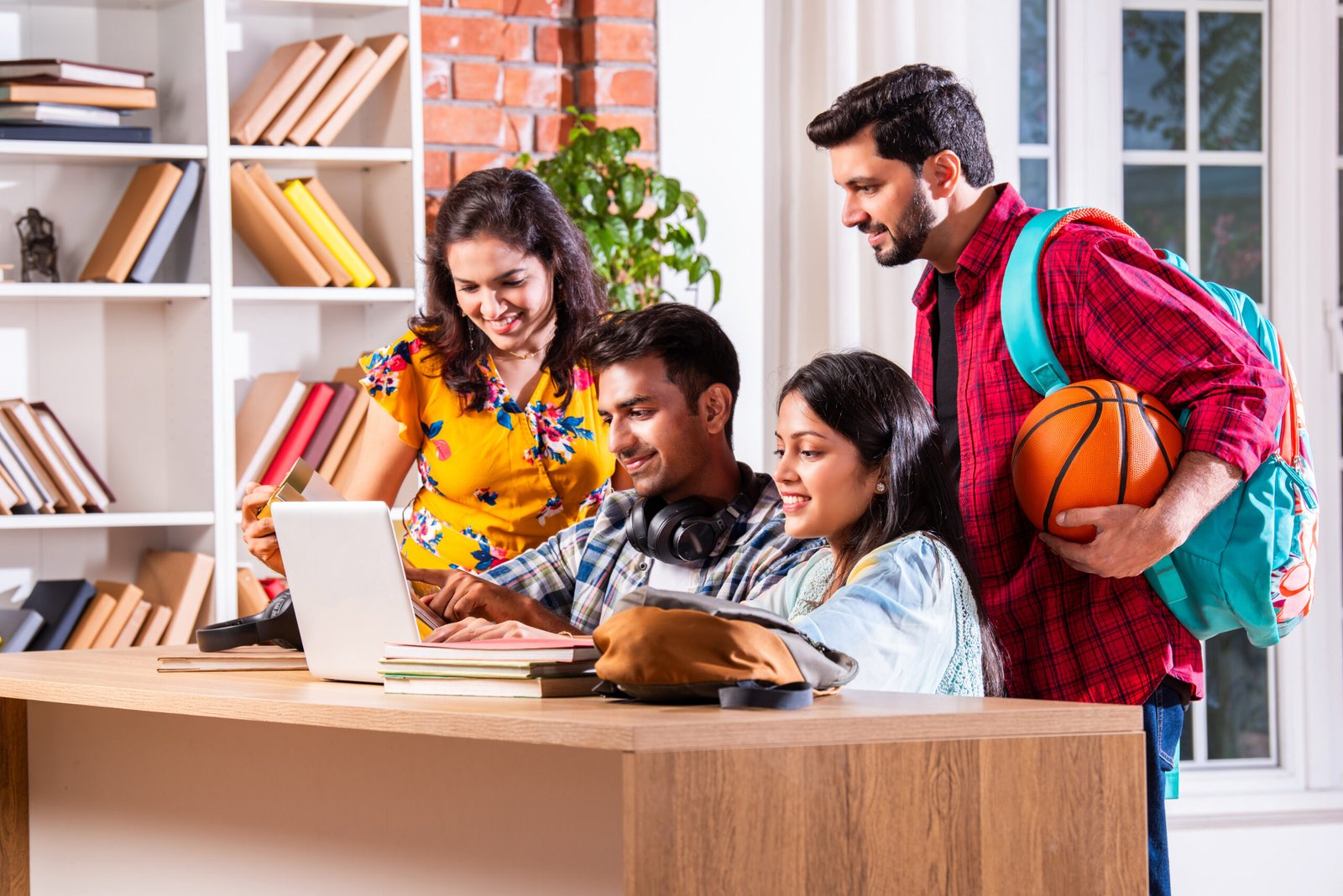 indian asian college or university students using laptop while sitting at table in library. group study for school assignment. pointing, taking selfie showing thumbs up or celebrating success